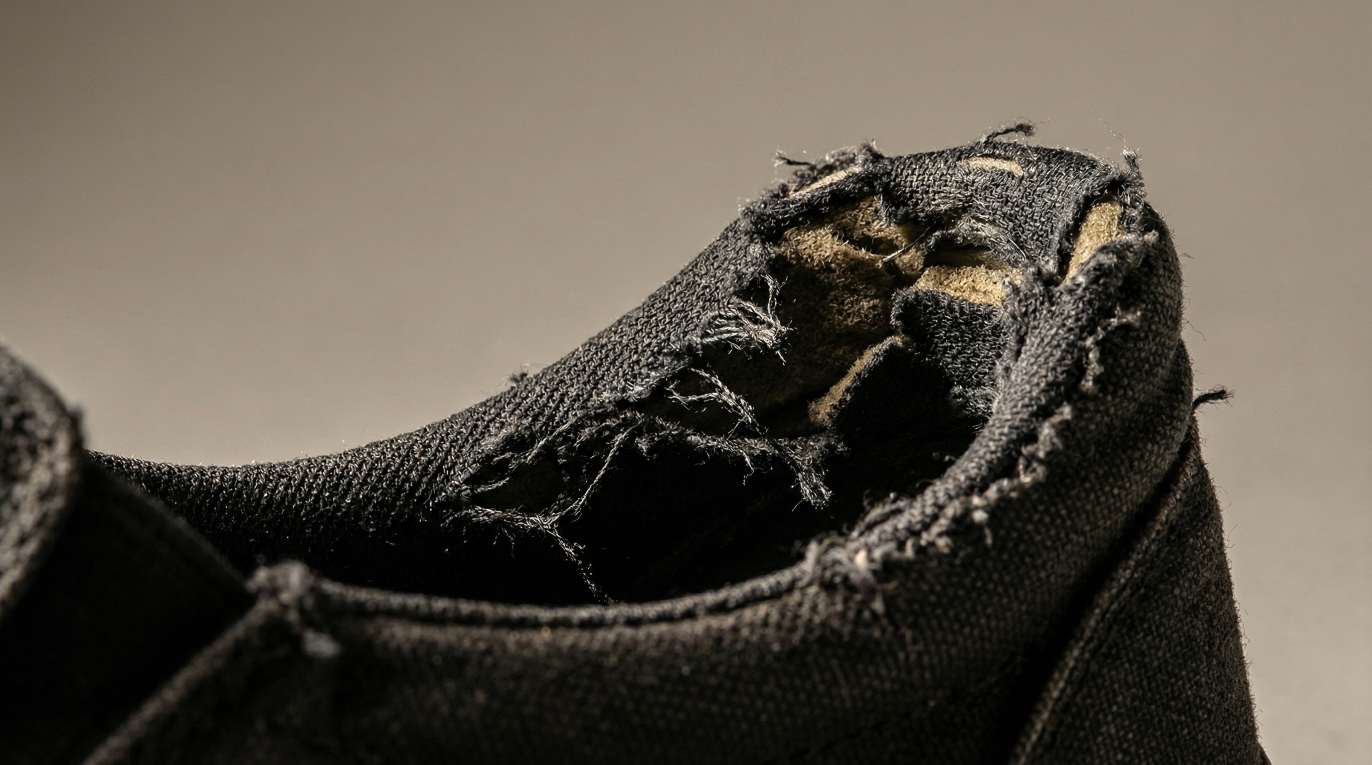 Close up view of a worn shoe heel showing frayed interior fabric and structural collapse