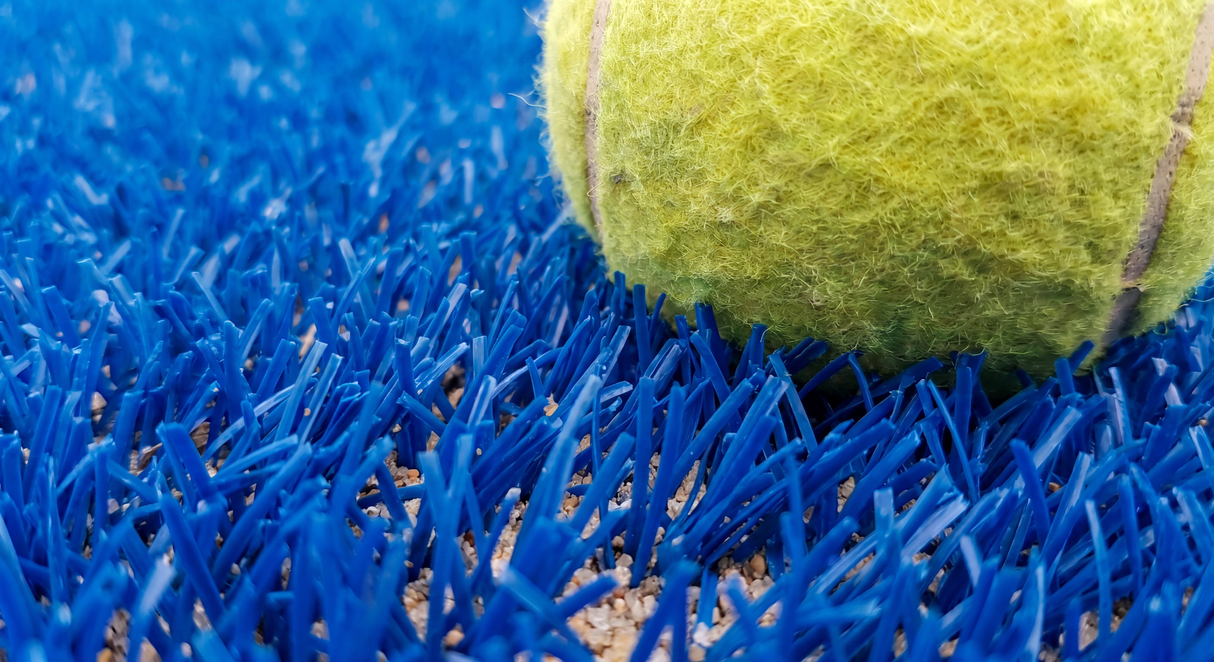 A macro shot of a yellow padel ball resting on professional blue artificial turf
