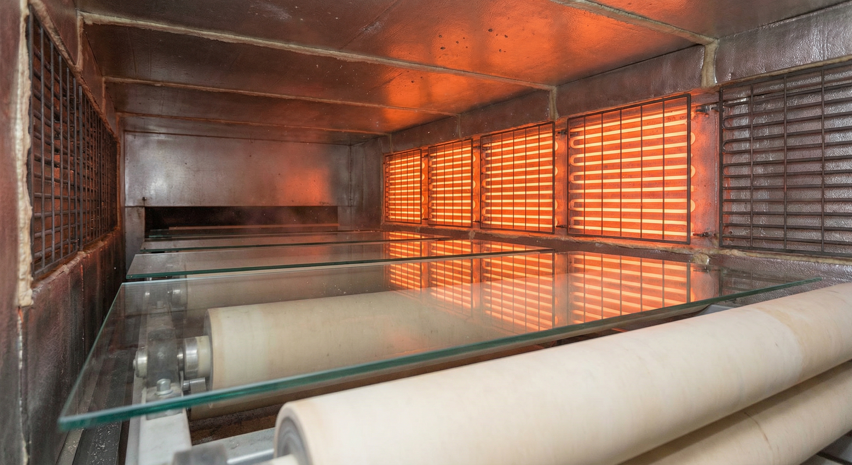 Interior view of a modern industrial horizontal glass tempering furnace with ceramic rollers and heating elements.