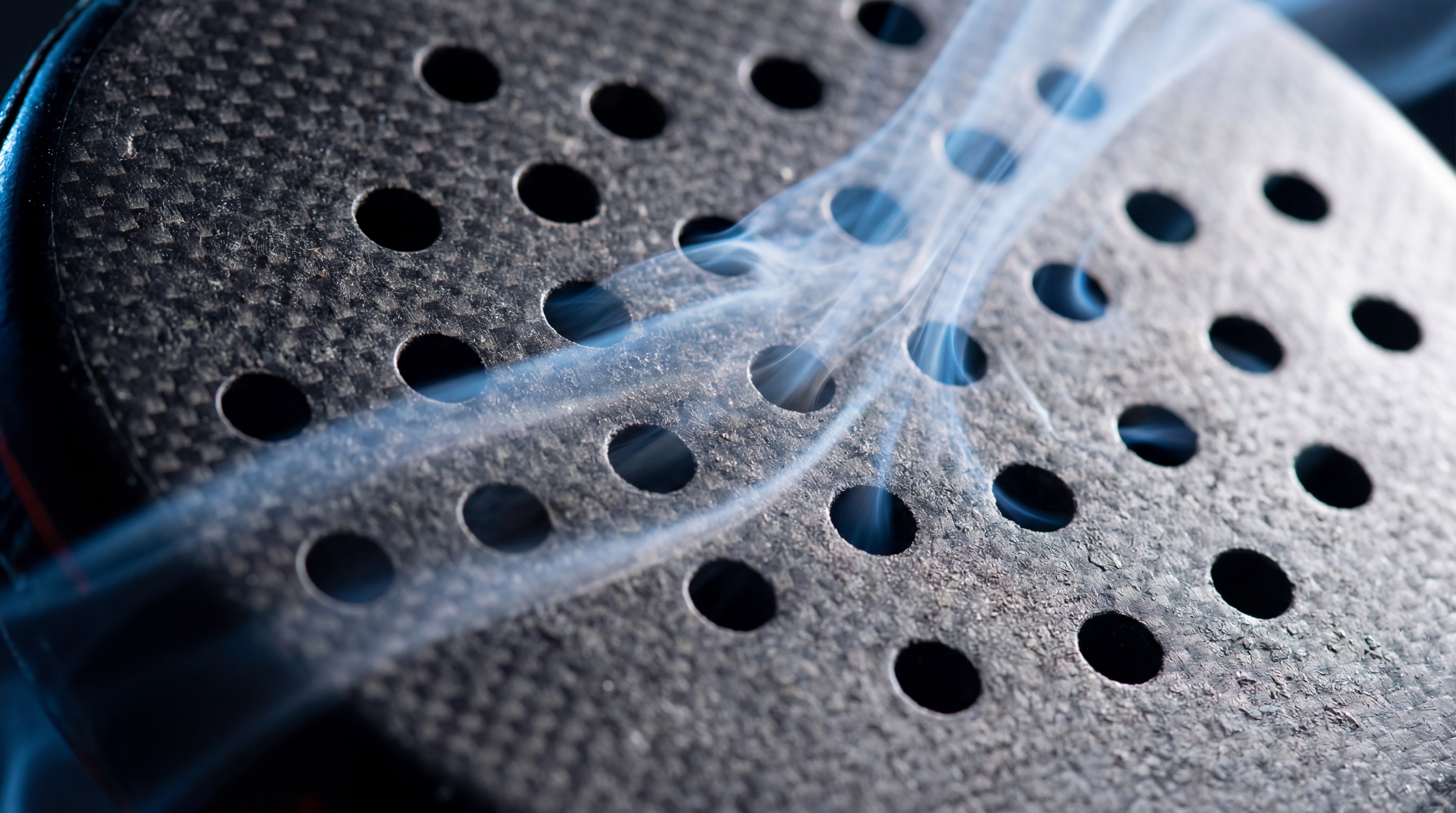 A photorealistic, high-speed action shot of a padel bat mid-swing, with visible trails of air flowing through the perforation holes.