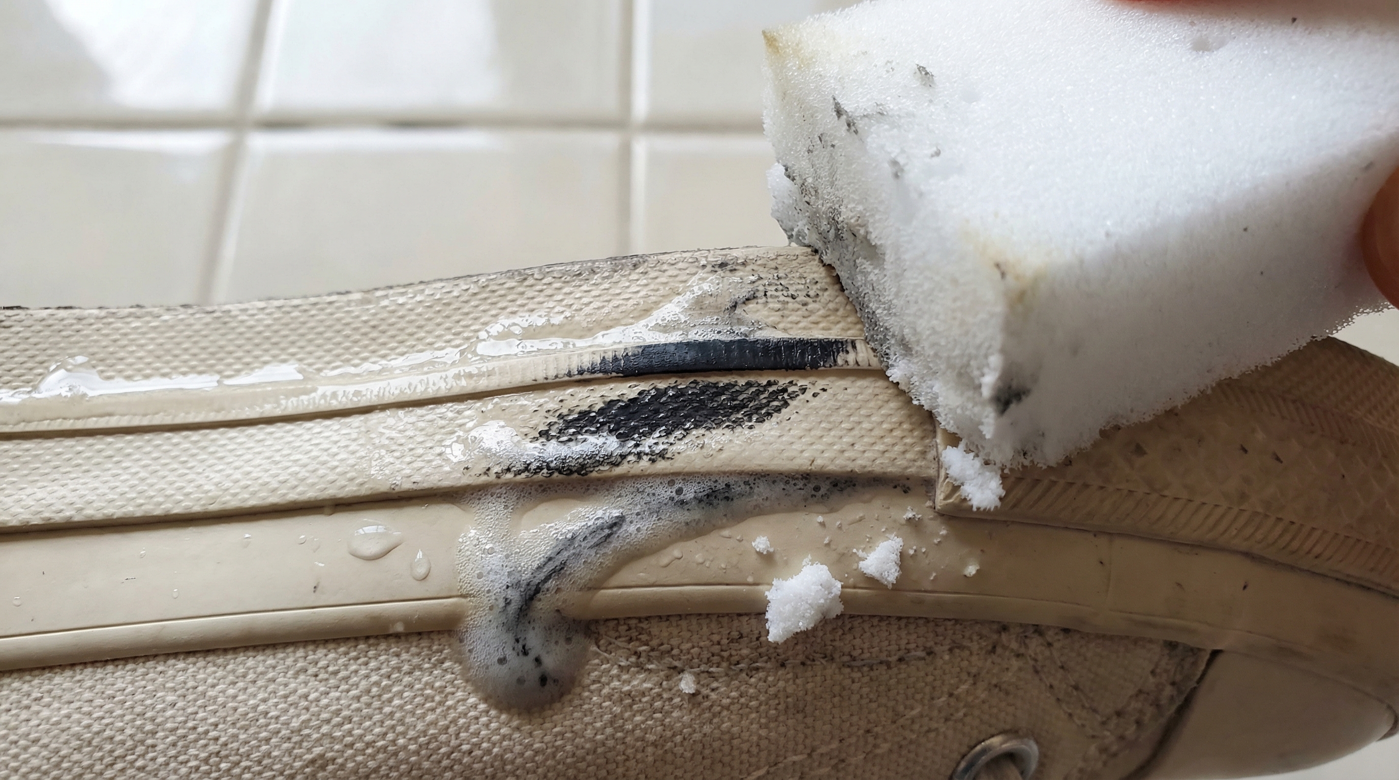 White melamine sponge erasing a scuff from the rubber of a canvas shoe