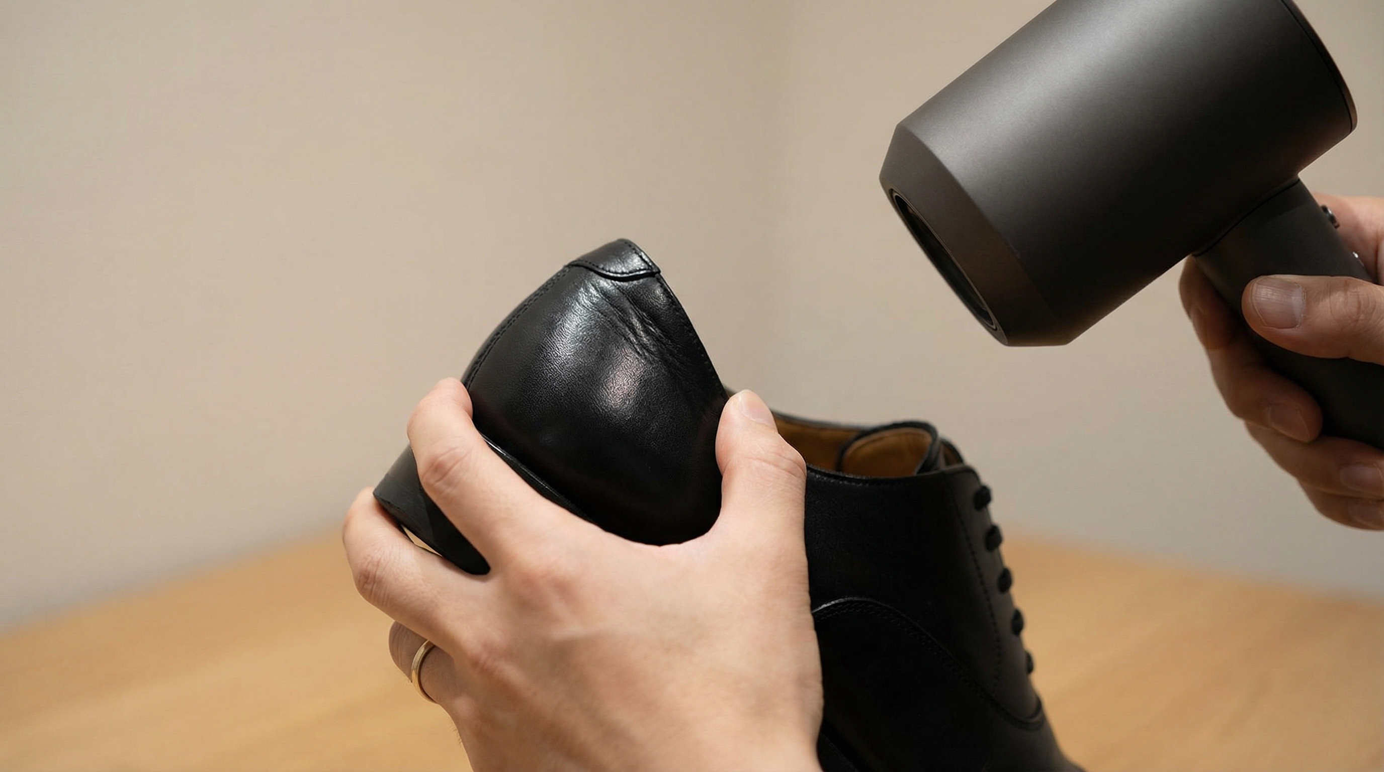 A close-up shot of a hairdryer blowing warm air onto the heel of a leather dress shoe with a hand inside the shoe flexing the material
