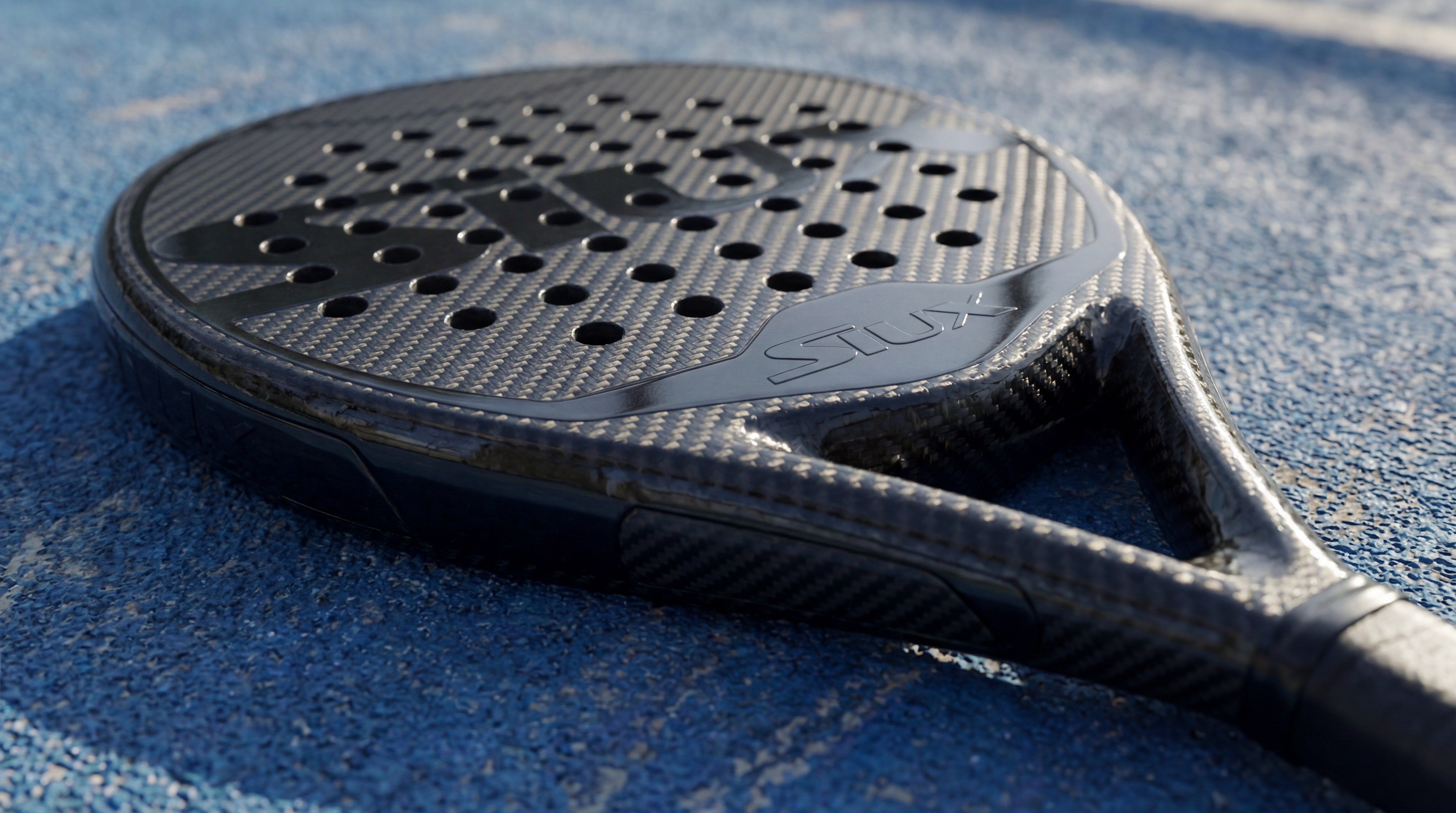 A photorealistic close-up of a professional Siux padel racket resting on a pristine blue World Padel Tour court, highlighting the intricate carbon weave and the sleek logo.