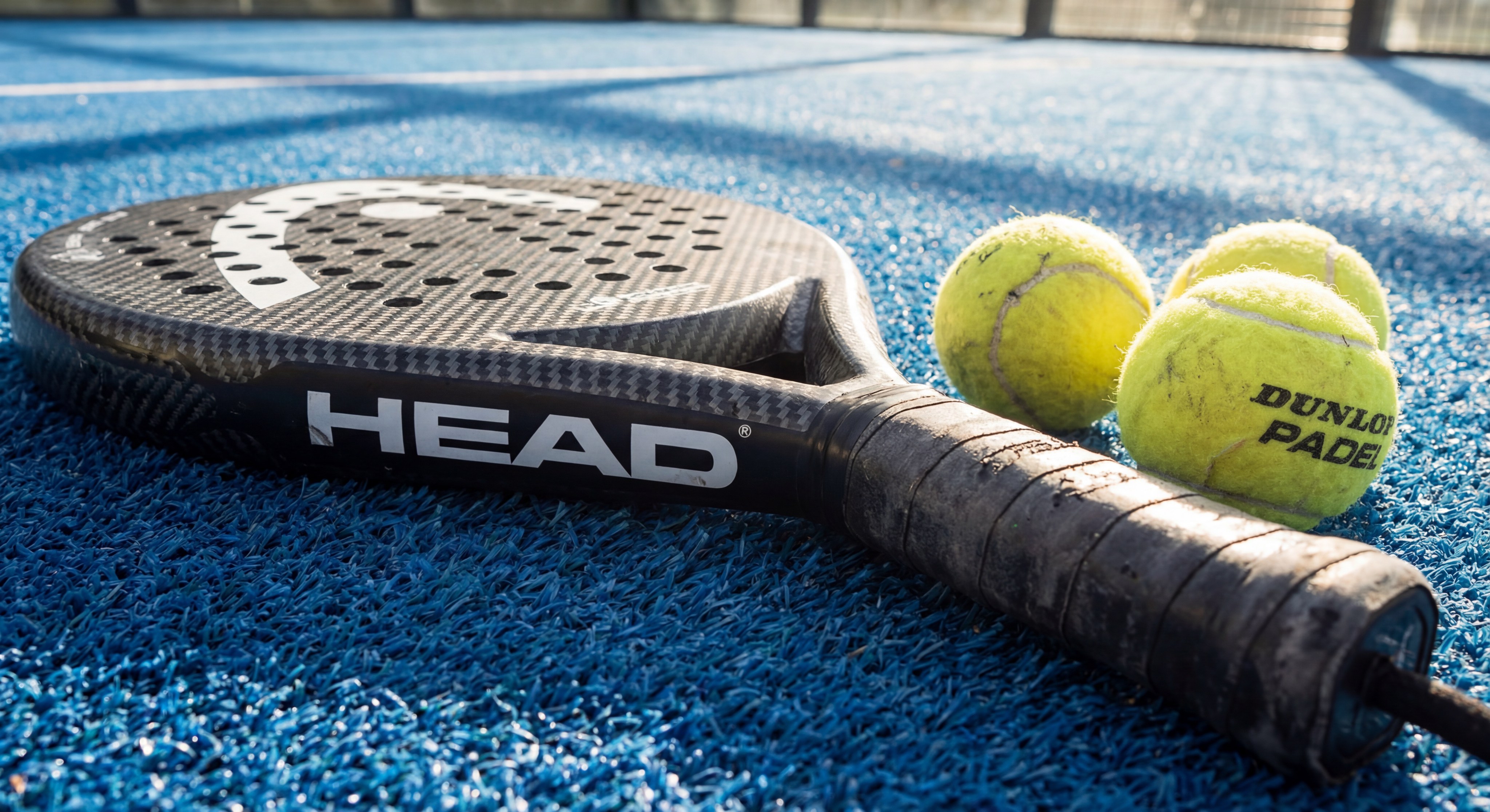 Professional padel racket and balls resting on a blue turf court.