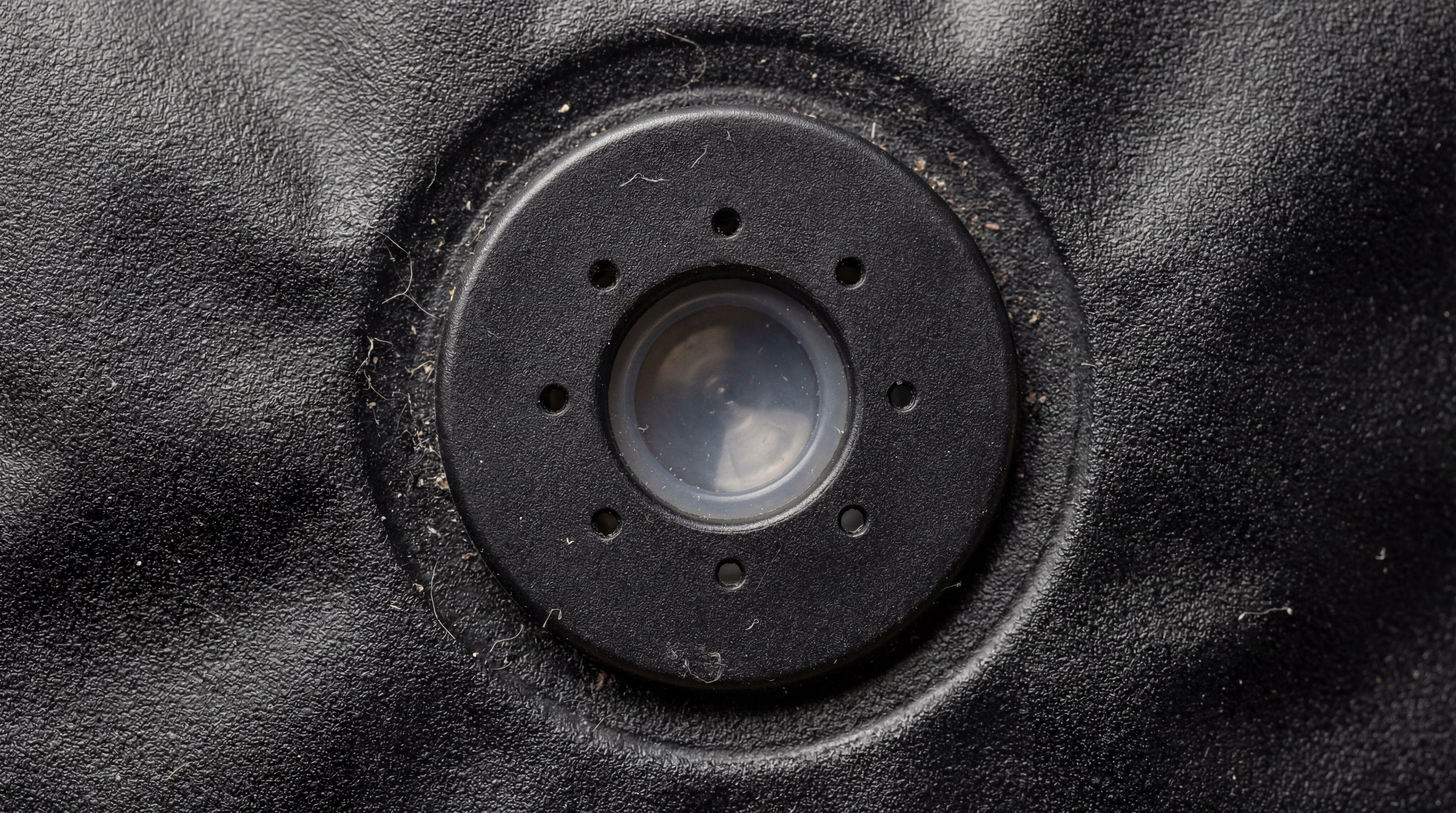 Macro photography of a one-way degassing valve integrated into a textured black coffee bag, showing the precise circular vents and the silicone diaphragm inside.