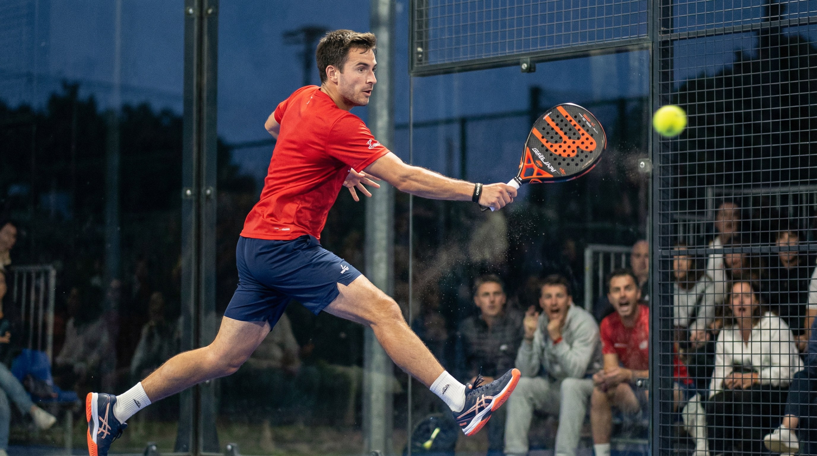 Action shot of a player hitting a padel ball with a backhand slice, with the ball caught in a slight motion blur.