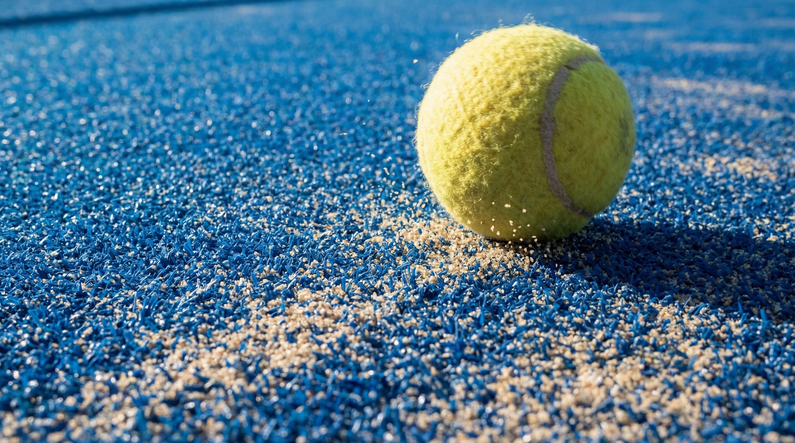 Wide shot of a panoramic padel court showing the glass walls and the blue artificial grass surface under bright stadium lights.