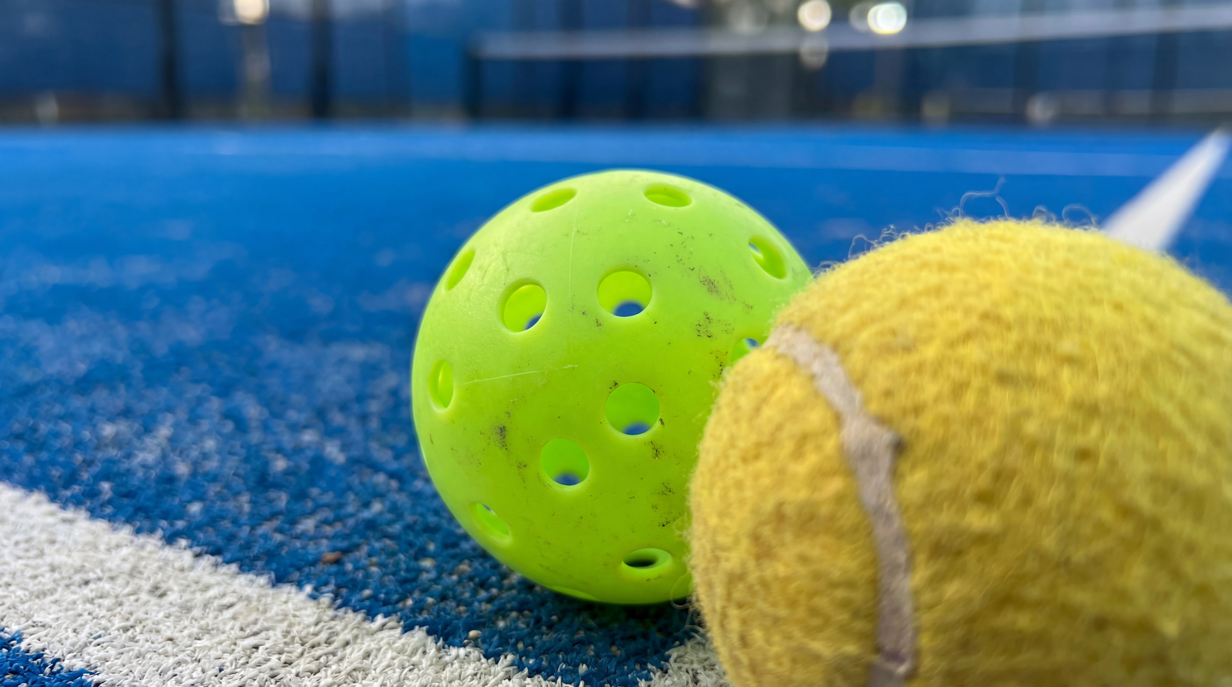 Padel ball and pickleball side-by-side on court surface
