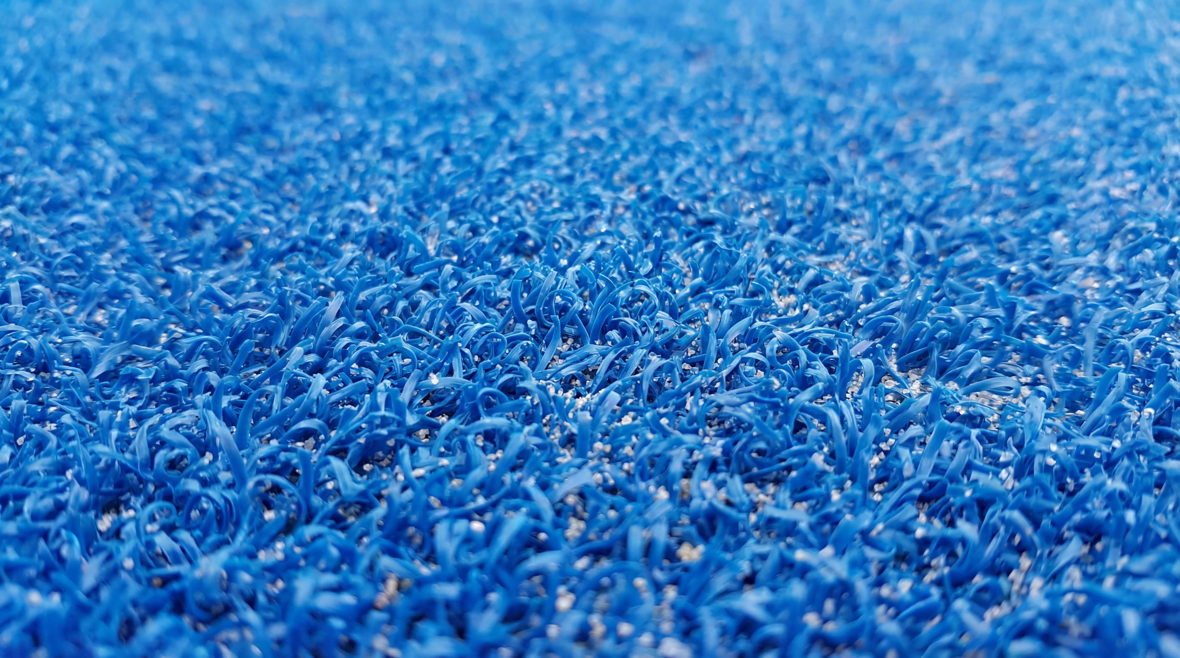 A photorealistic shot of high-density blue fibrillated padel grass with a thin layer of silica sand.