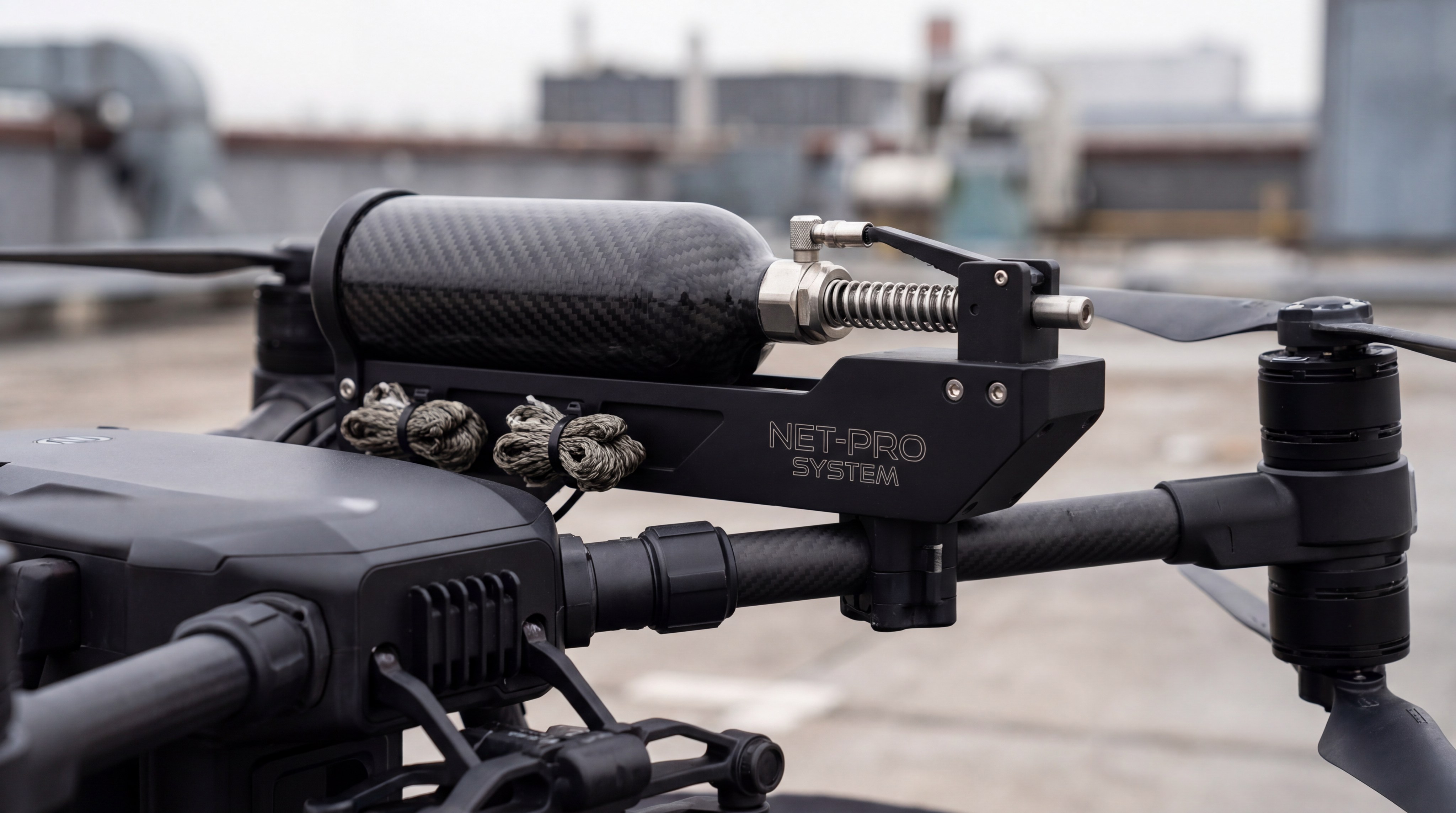 A detailed close-up of a carbon-fiber net projectile launcher mounted on a professional security drone
