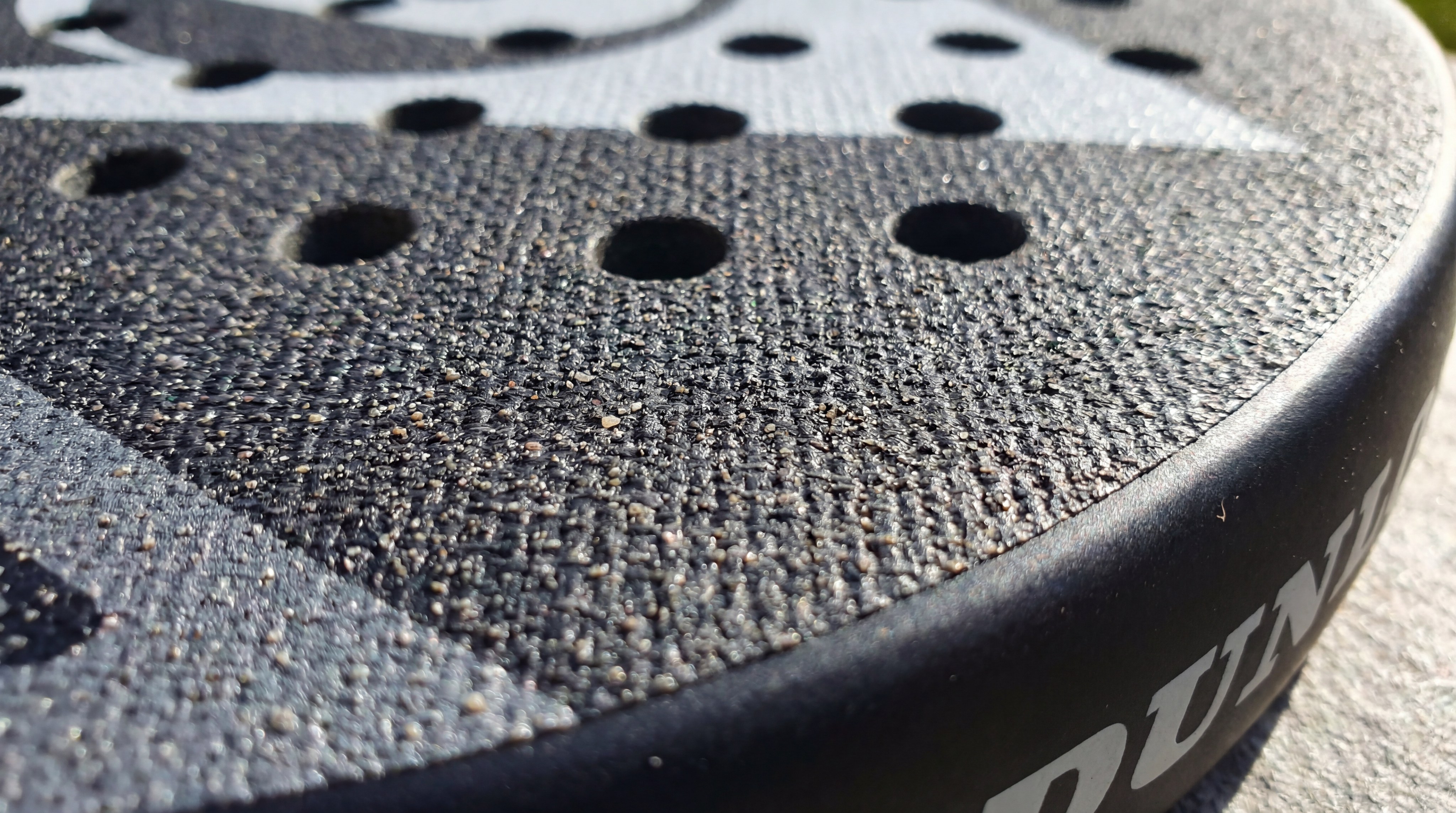 A macro photorealistic shot of the surface of a Siux racket, showing the "Sandy" finish and 3D relief patterns that grip the ball.