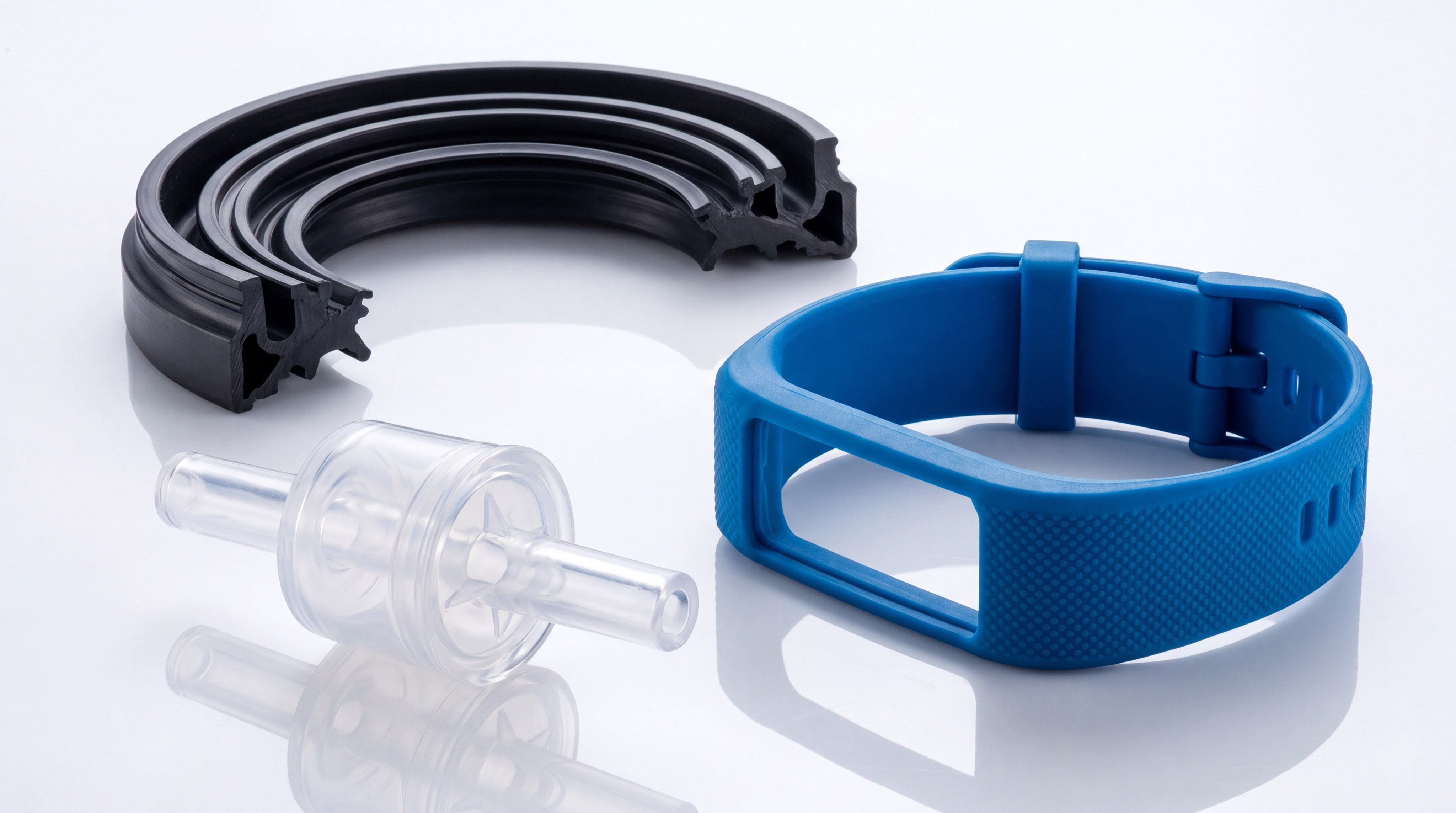 A macro shot of various finished LSR components: a translucent medical valve, a wearable strap, and an automotive seal.