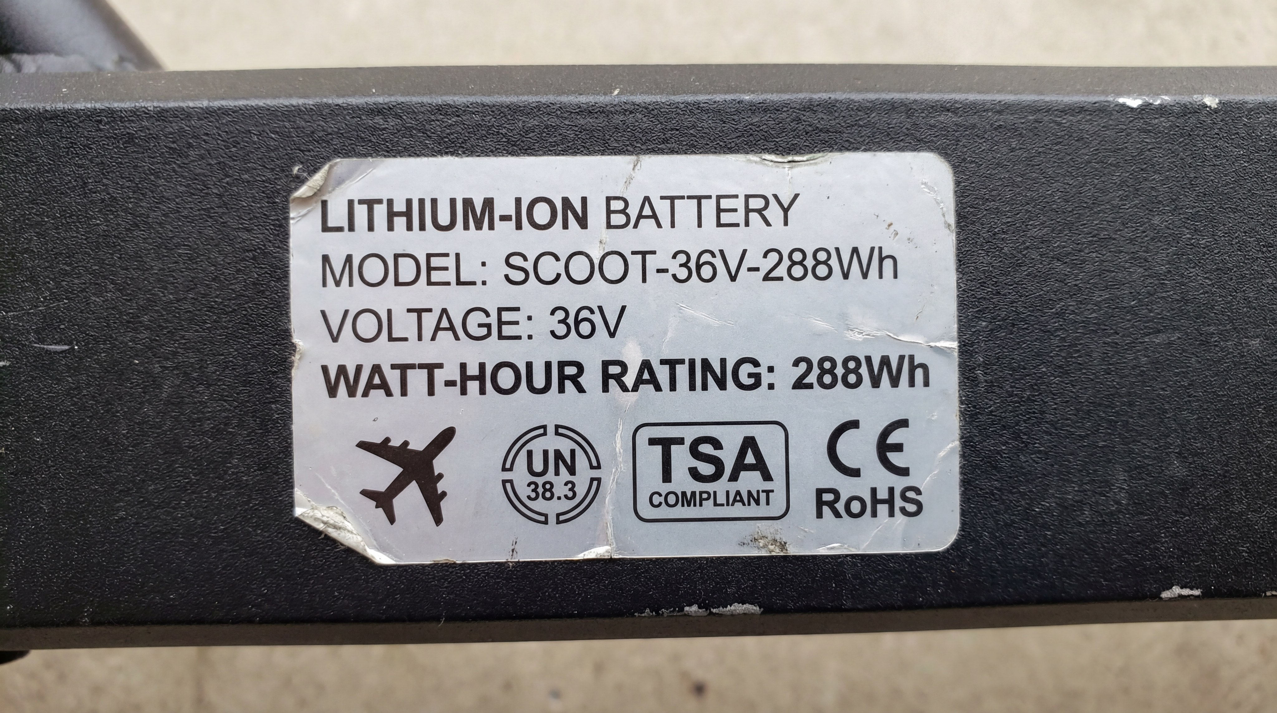 A close-up of a lithium-ion battery specification label on a scooter deck, highlighting the Watt-hour (Wh) rating for travel compliance.
