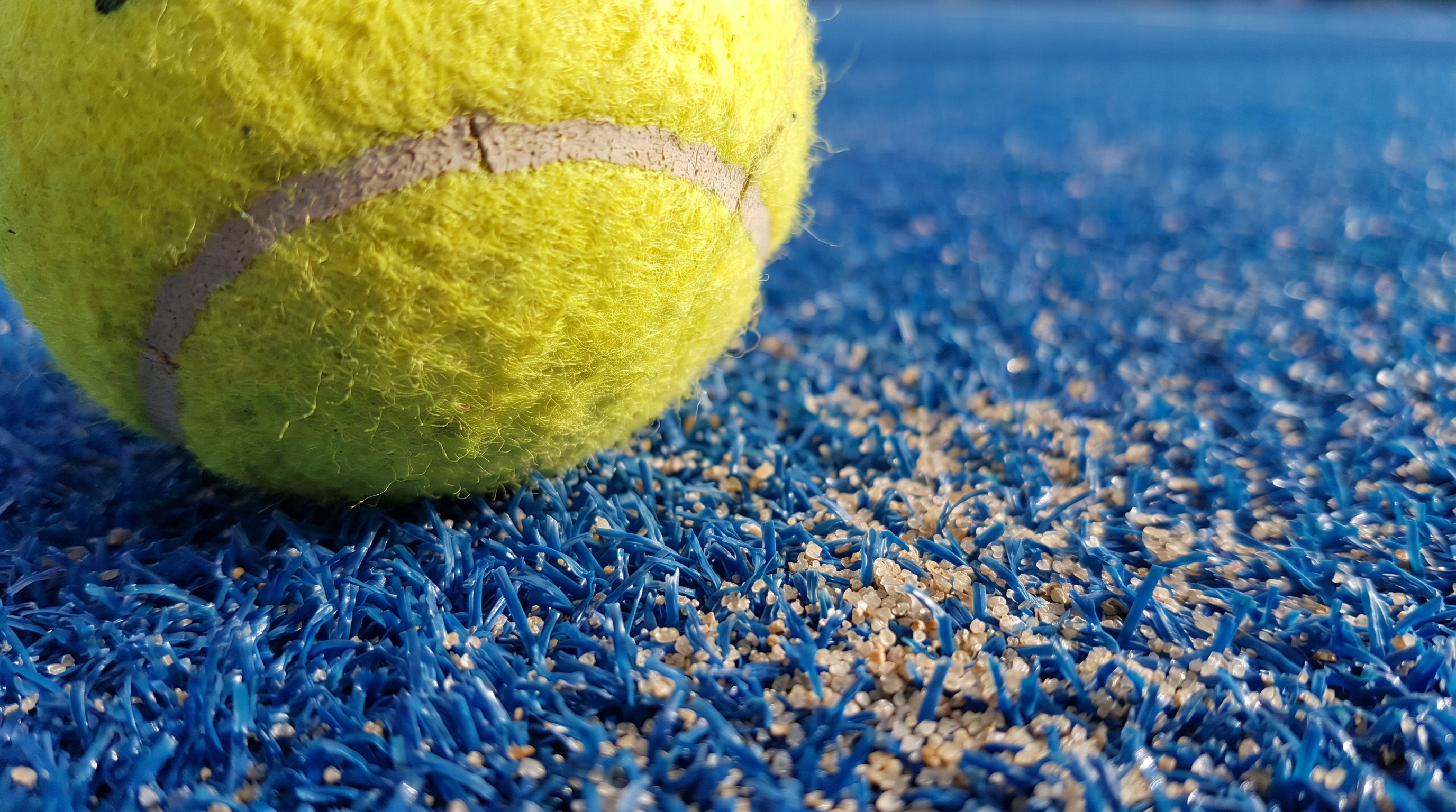 Macro shot of professional blue padel turf with a yellow ball.