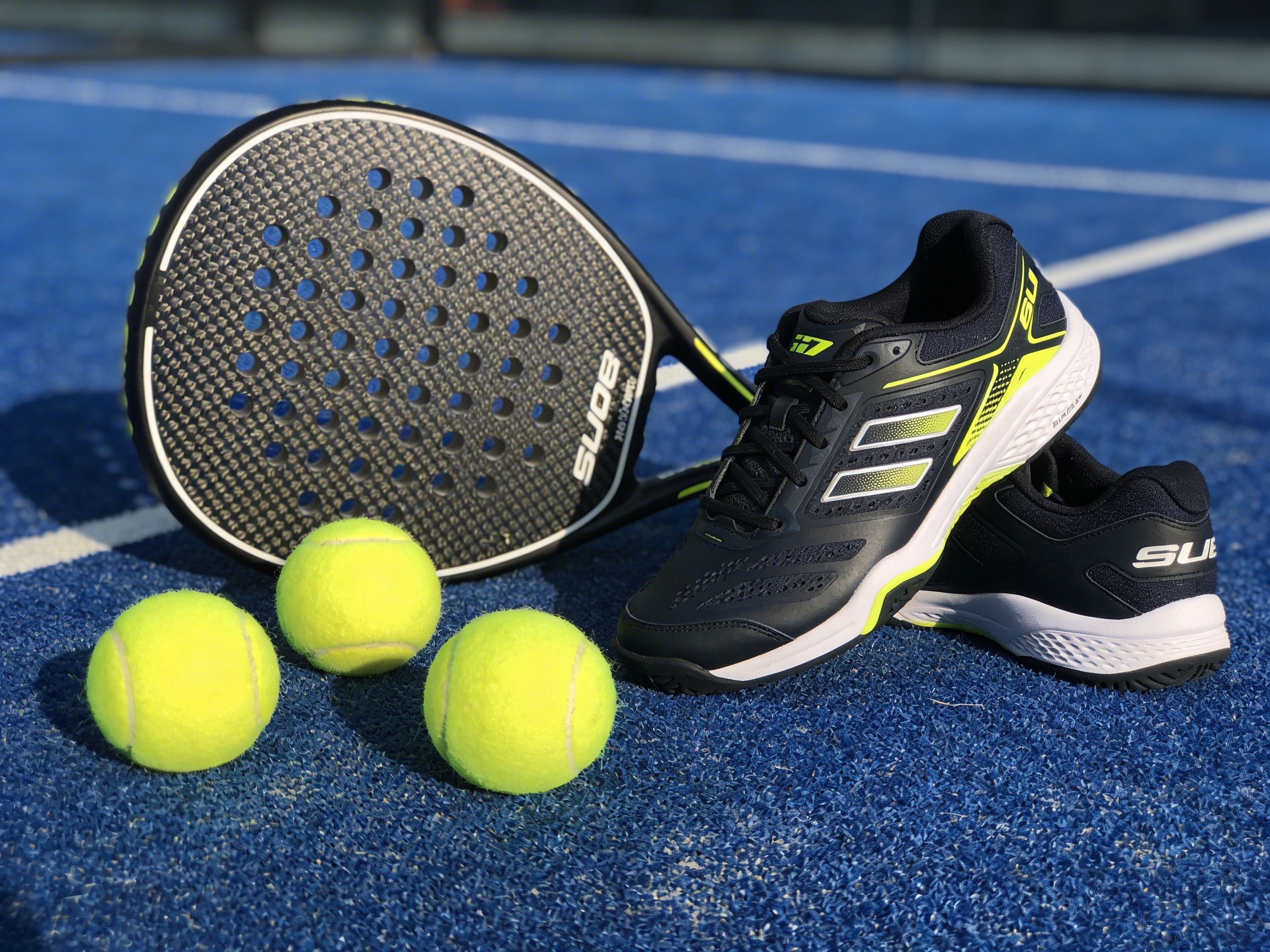A photorealistic flatlay showing a professional carbon fiber padel racket, balls, and specialized shoes.
